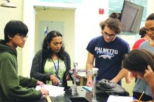 Sophomore Thomas Toomey (left) and senior Nicholas Zajac present their lab work to Ms. Joseph (center).