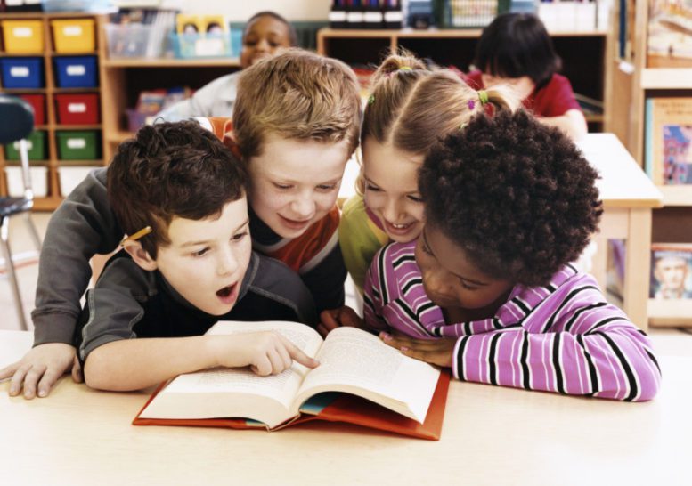 Girls and Boys Looking at the Same Textbook in a Classroom at Primary School