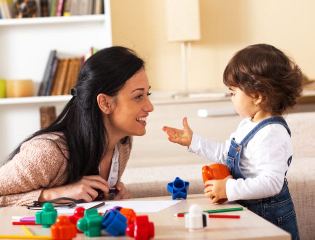 Mother and baby girl playing with toys in living room.