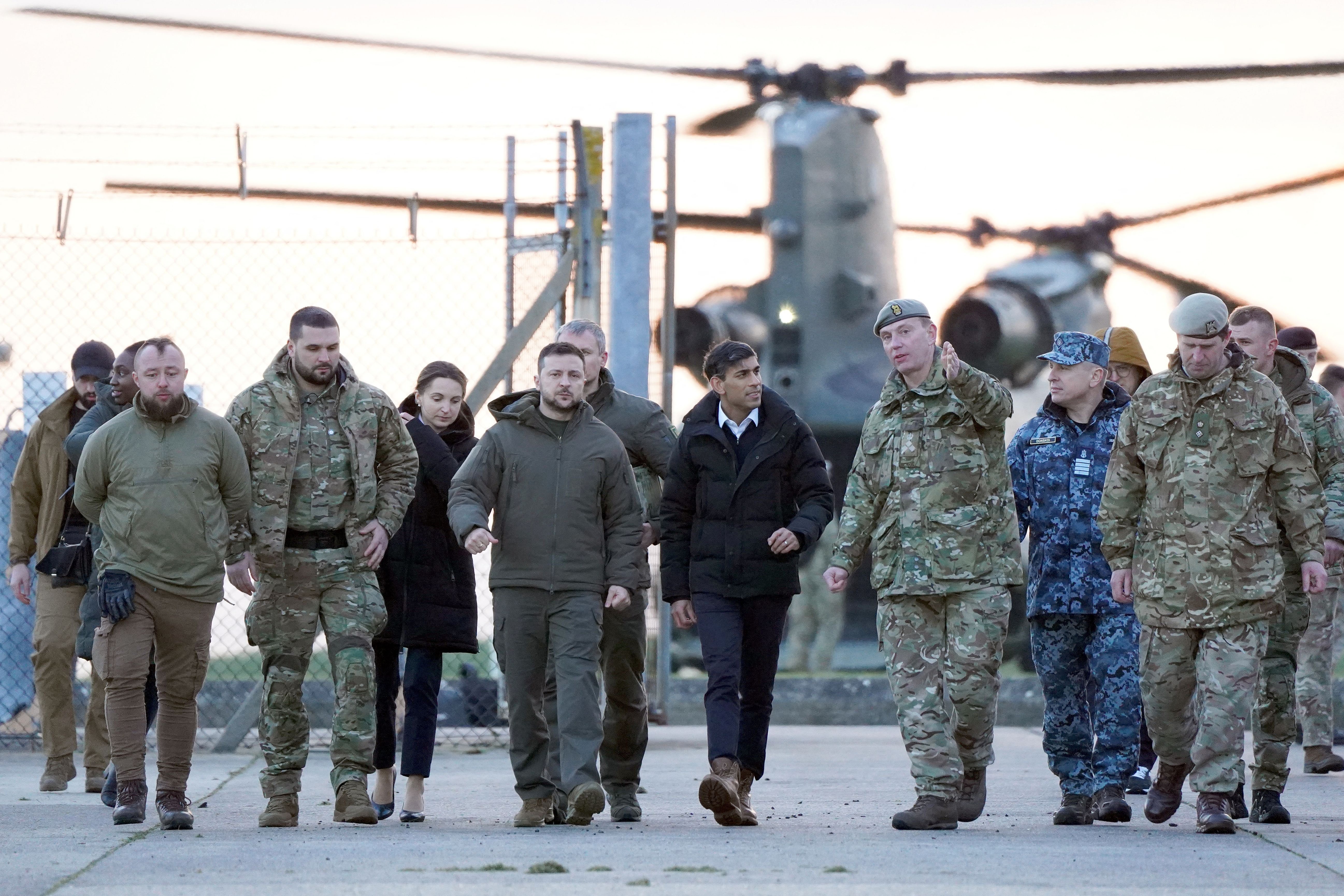 A group of mostly men in drab military garb walk toward the camera.