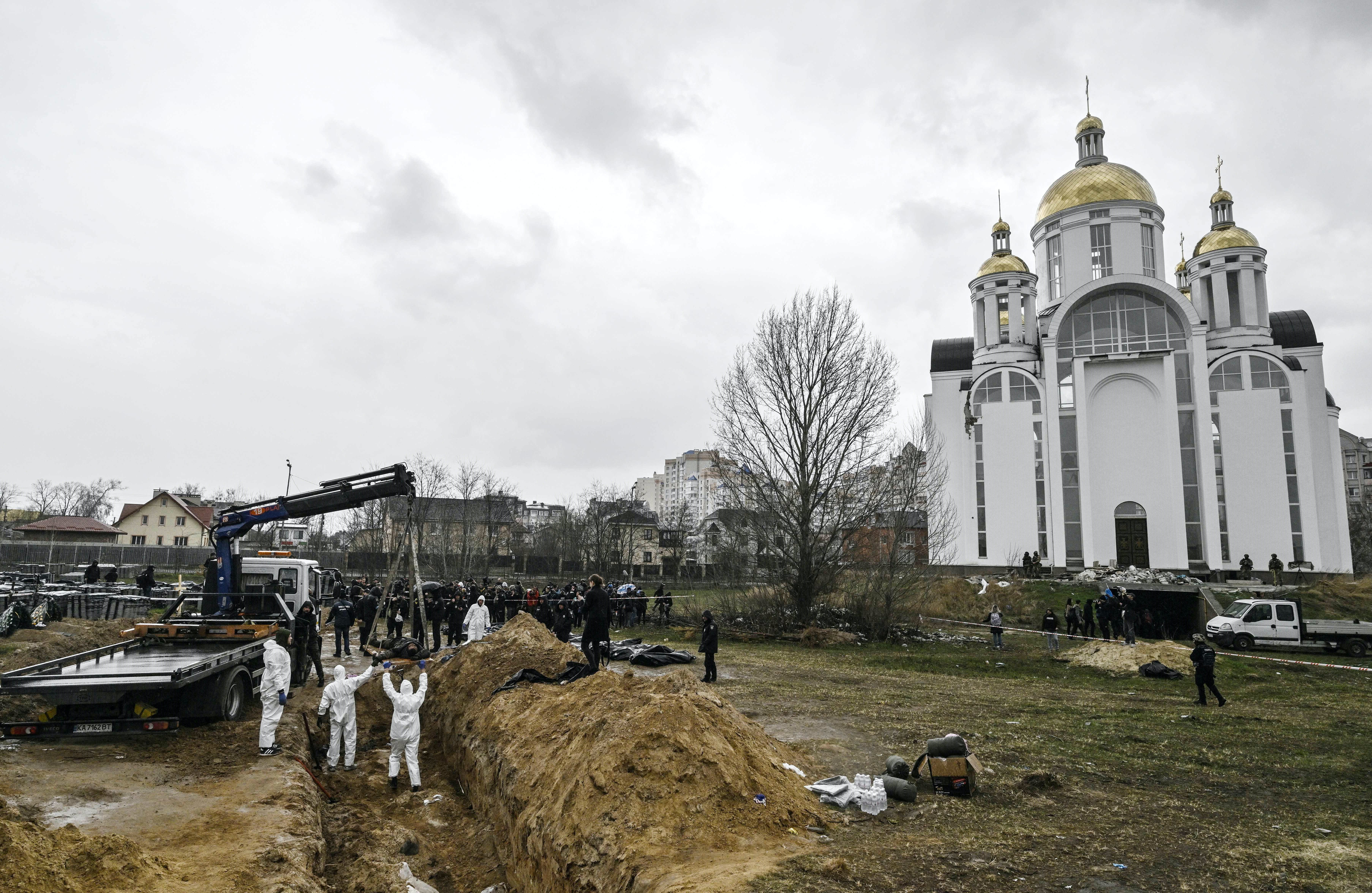 People in white appear to be digging in a large trench, outside of a white church.