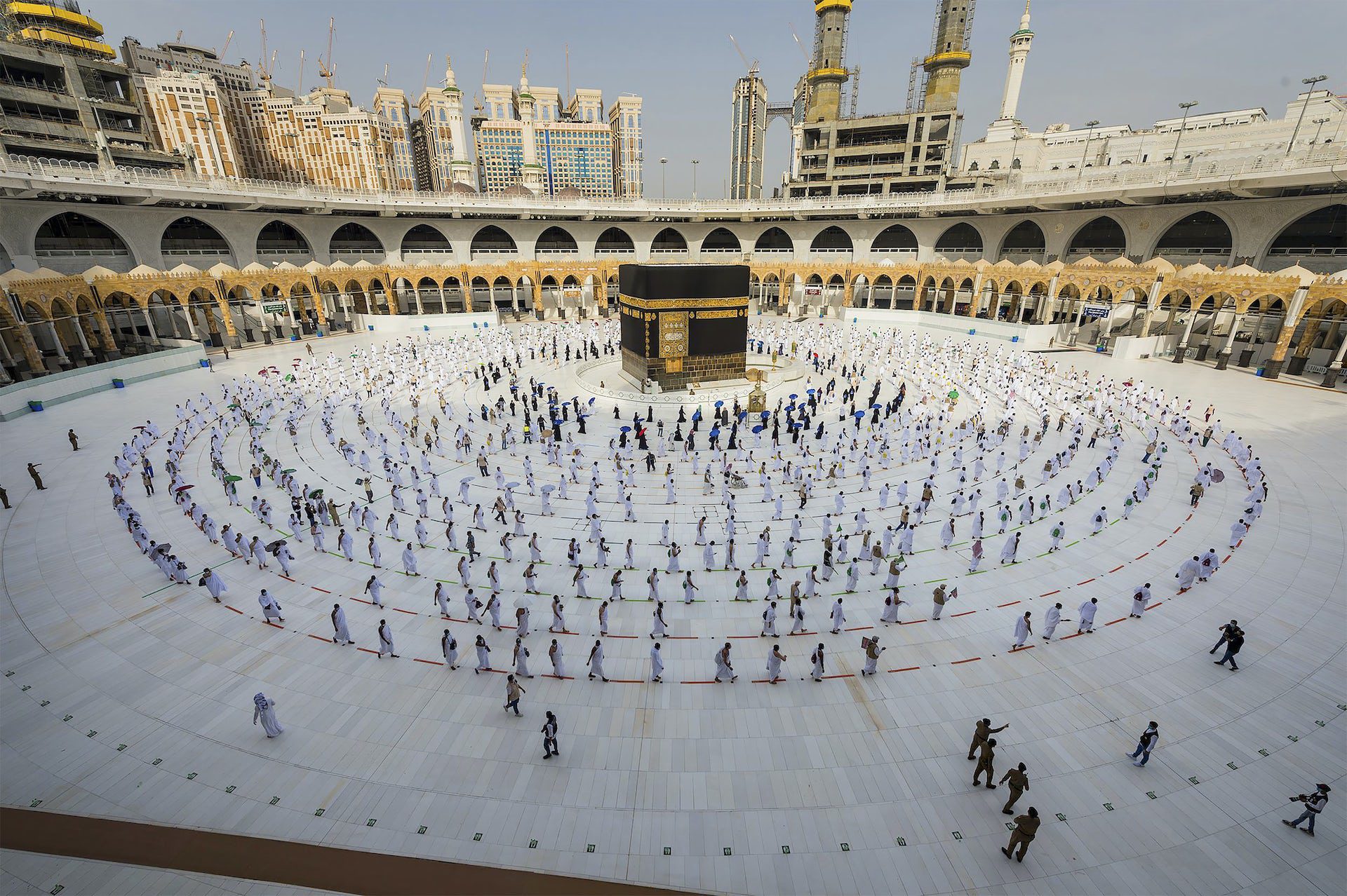 People walk around a black cubic structure along circular rows.