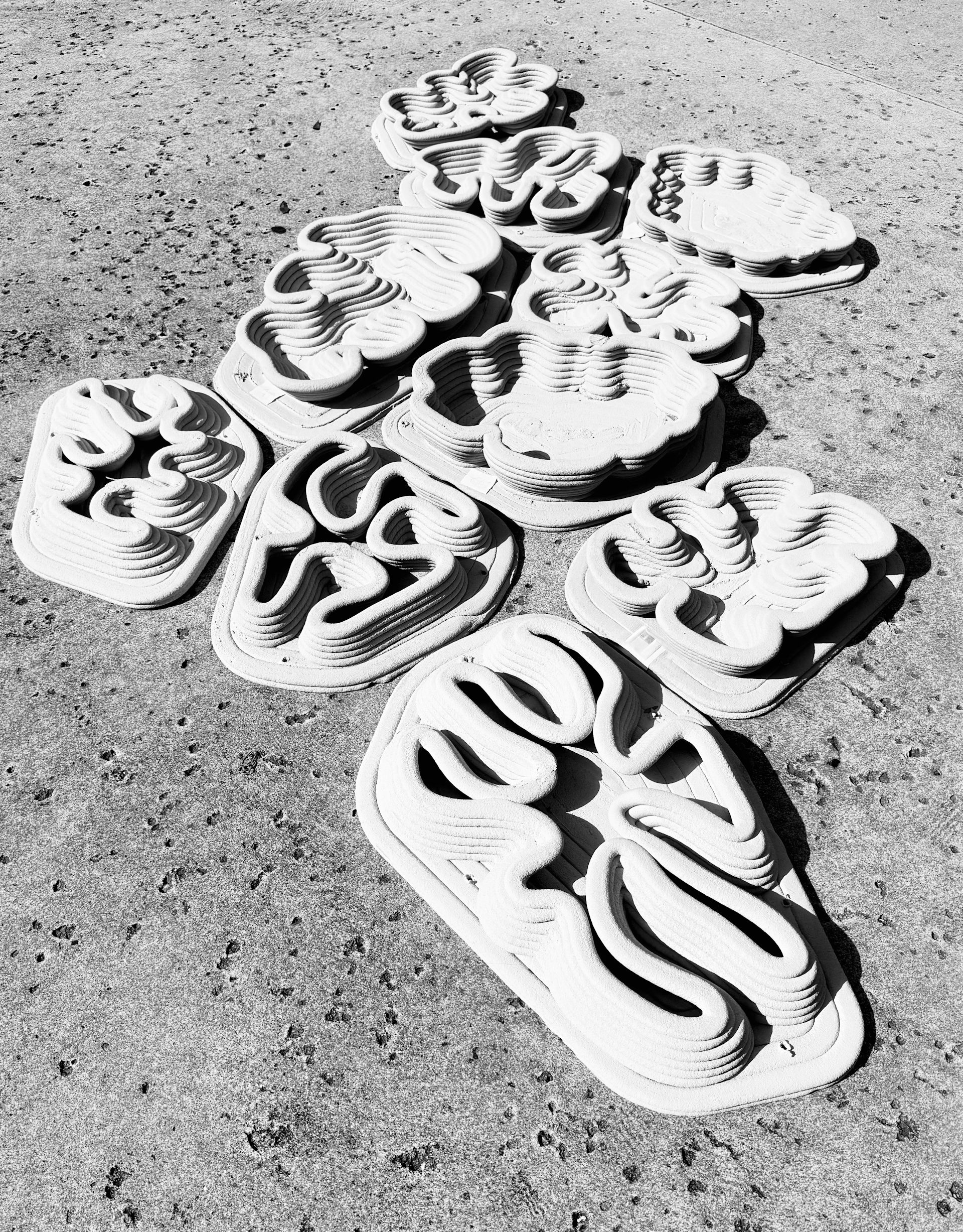 Ten grey swirling organically shaped objects laid together on ground