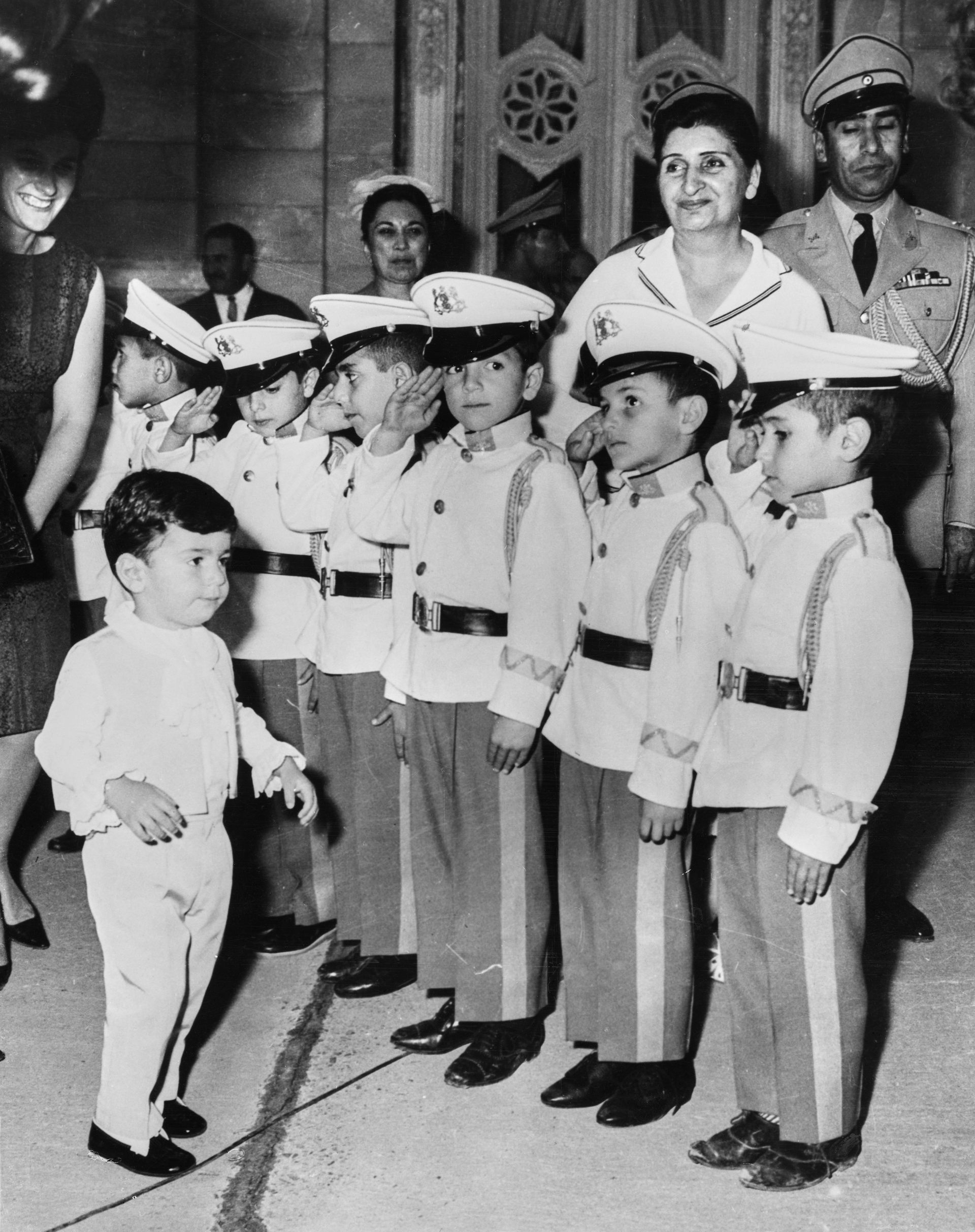 A young boy standing in front of a line of boys in military uniforms.